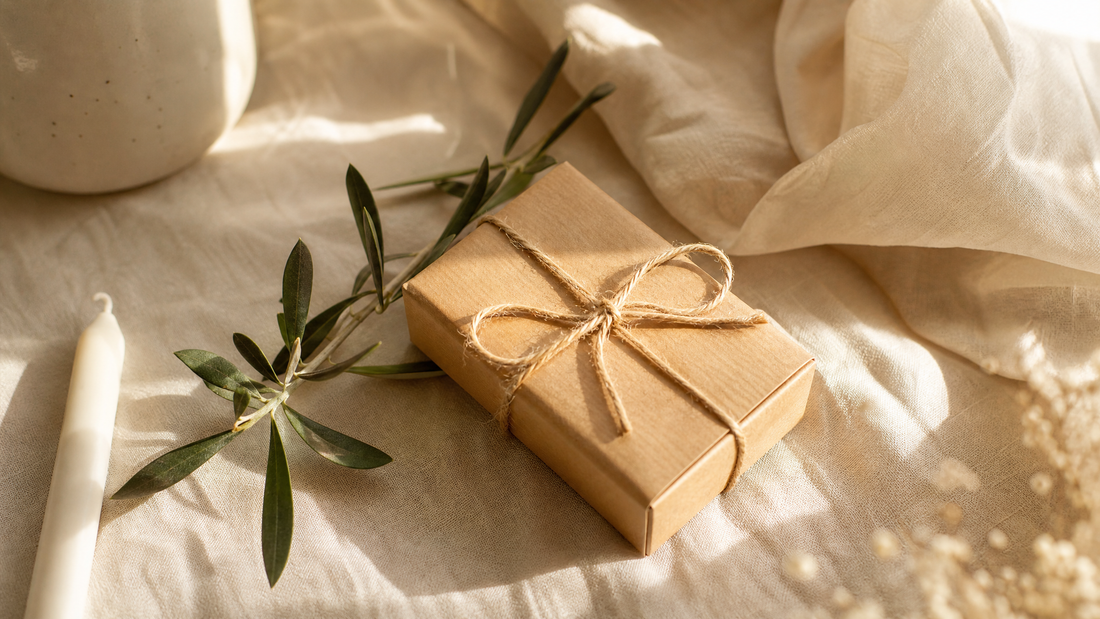 A small gift wrapped in kraft paper and twine beside a candle and olive branch