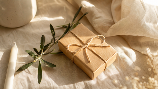 A small gift wrapped in kraft paper and twine beside a candle and olive branch
